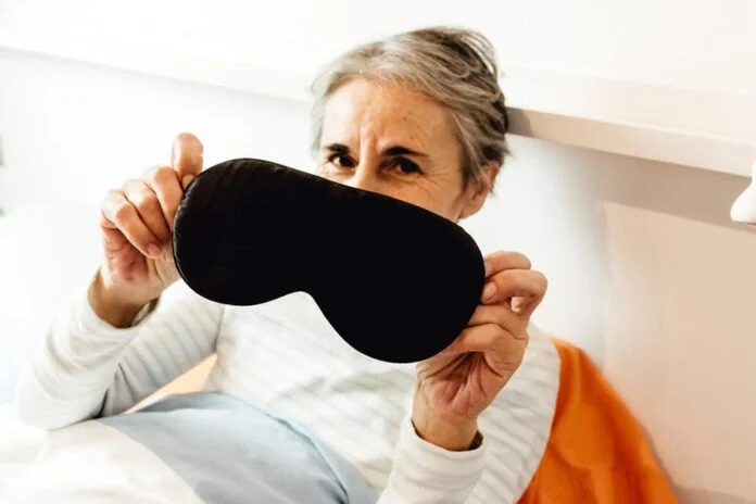 person in bed holds their eye mask for the camera - Image of Health and Wellness, sleep aid products